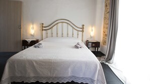 Una cama bien tendida con una colcha blanca y dos toallas enrolladas, flanqueada por mesitas de noche con lámparas, en una habitación de diseño sencillo y limpio.