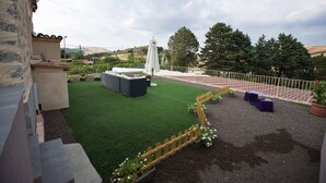 Un jardín en la azotea con césped artificial, zonas de estar y un área de juegos cercada.
