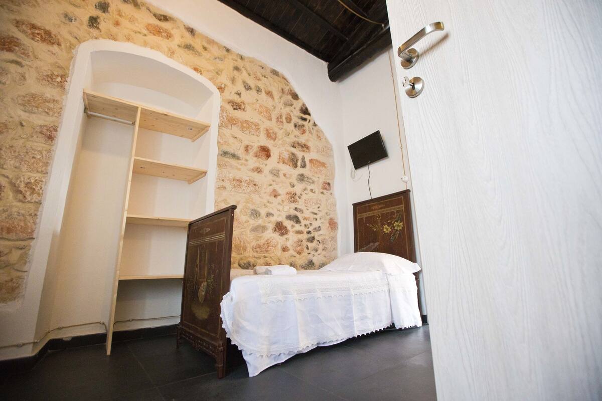 Ein Schlafzimmer mit Steinwand, Holzbettgestell, weißer Bettdecke und Holzschrank.