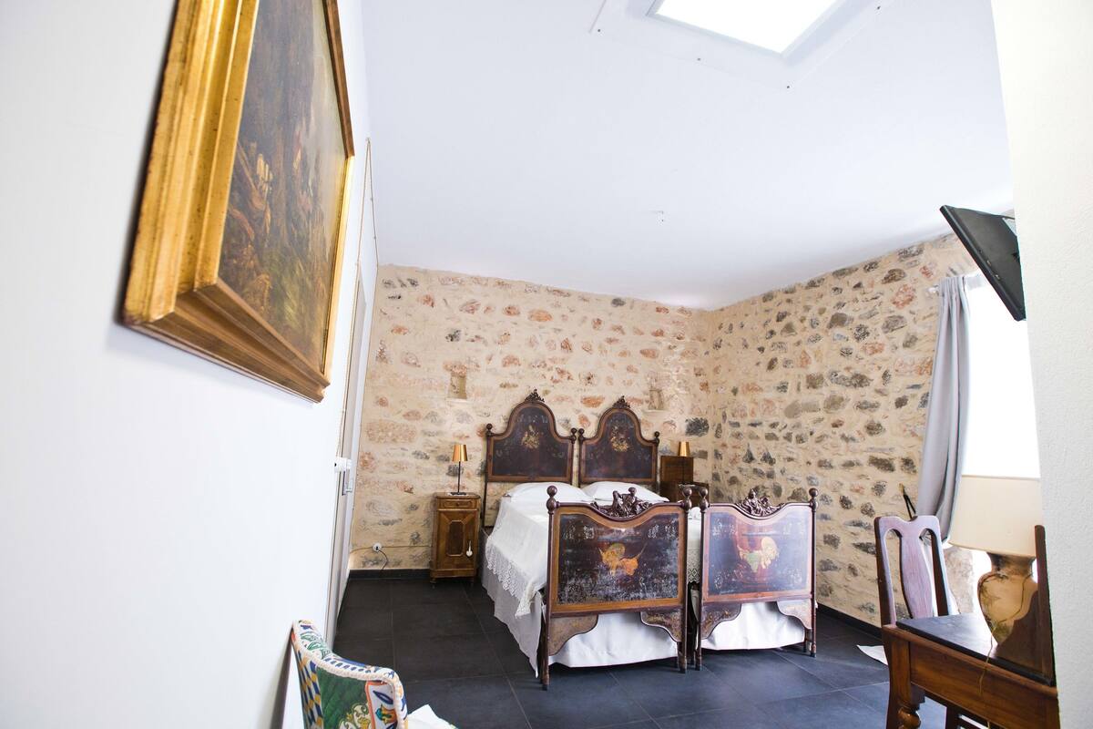 Ein Schlafzimmer mit Steinwand, einem Bett mit Holz-Kopfteil, einem Nachttisch, einem Sessel und einem Gemälde.