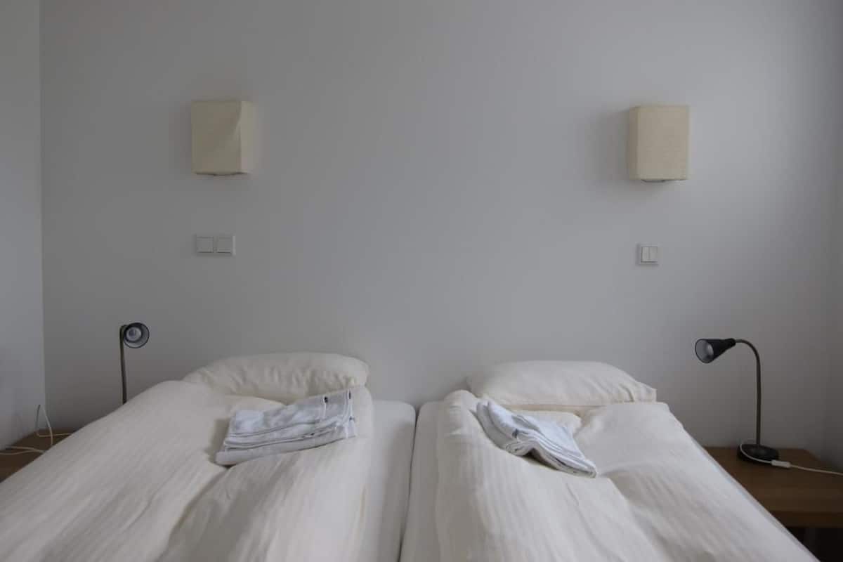 A simple, clean room with two beds, a bedside table with a lamp, and a wall-mounted light fixture.
