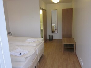 A bedroom with two beds, a wooden bench, a mirror, and a trash bin.