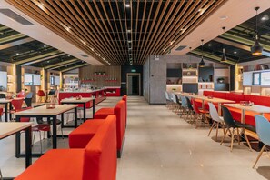 Um restaurante moderno com tetos altos, vigas aparentes e uma combinação de assentos vermelhos e azuis.
