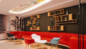 Ein modernes Interieur mit einem roten Sofa, mehreren Stühlen und Holzregalen mit Dekorationsobjekten.