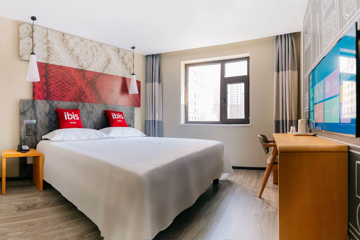 Habitación de hotel con una cama grande, un escritorio, un televisor y una ventana con cortinas.
