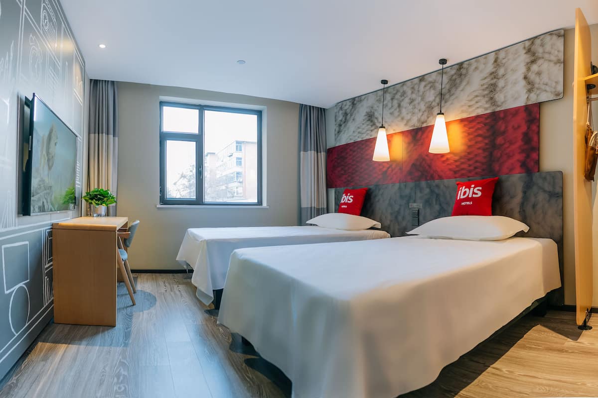 Una habitación de hotel con dos camas, un escritorio, una planta en maceta y un ventanal grande.