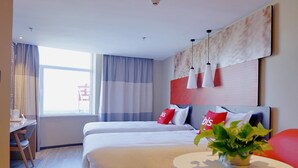 Habitación de hotel moderna con una cama grande, mesitas de noche, una pequeña mesa redonda con una planta y vistas al exterior.