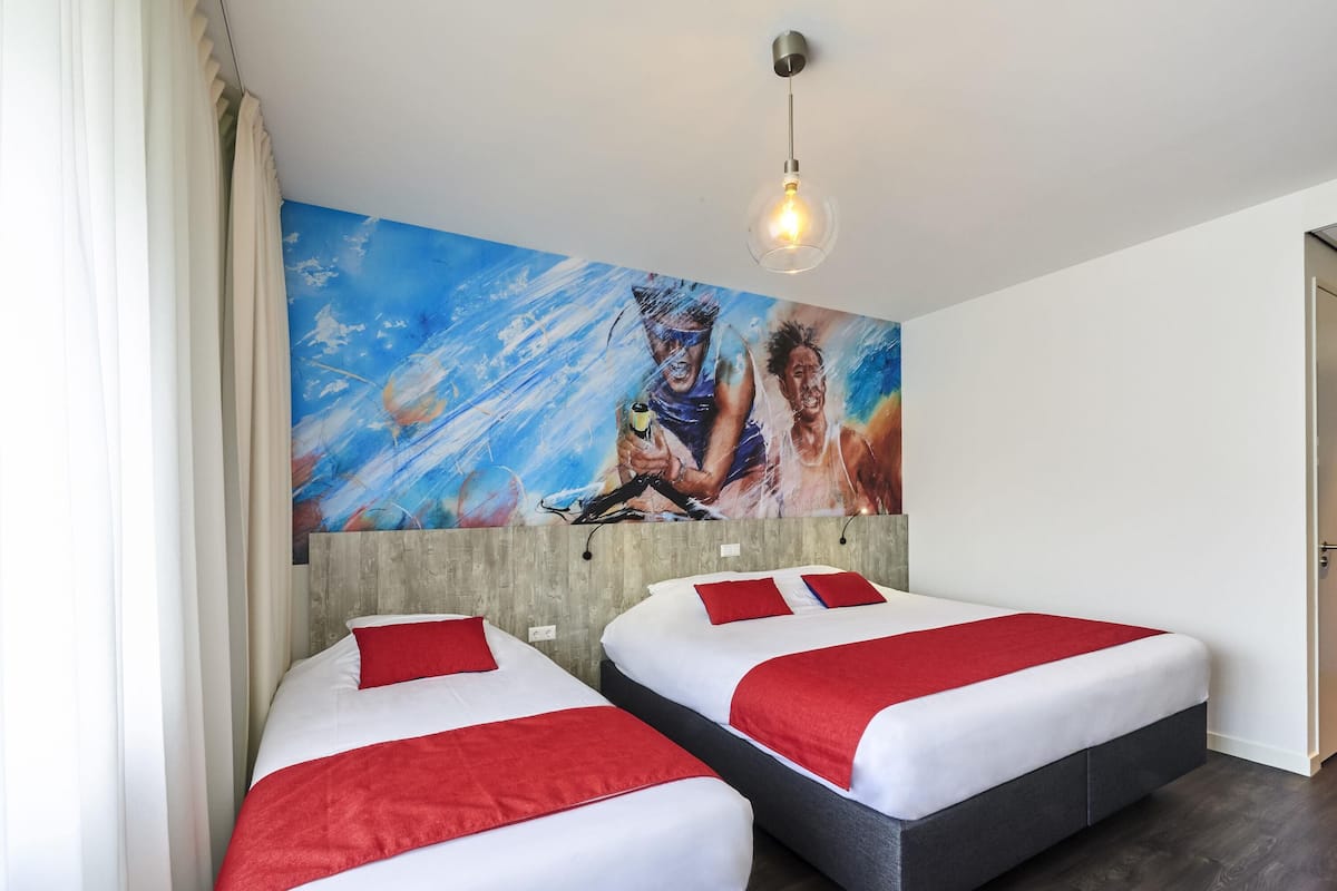 Habitación de hotel con dos camas, un cuadro abstracto grande en la pared, cabecera de madera y lámpara colgante.