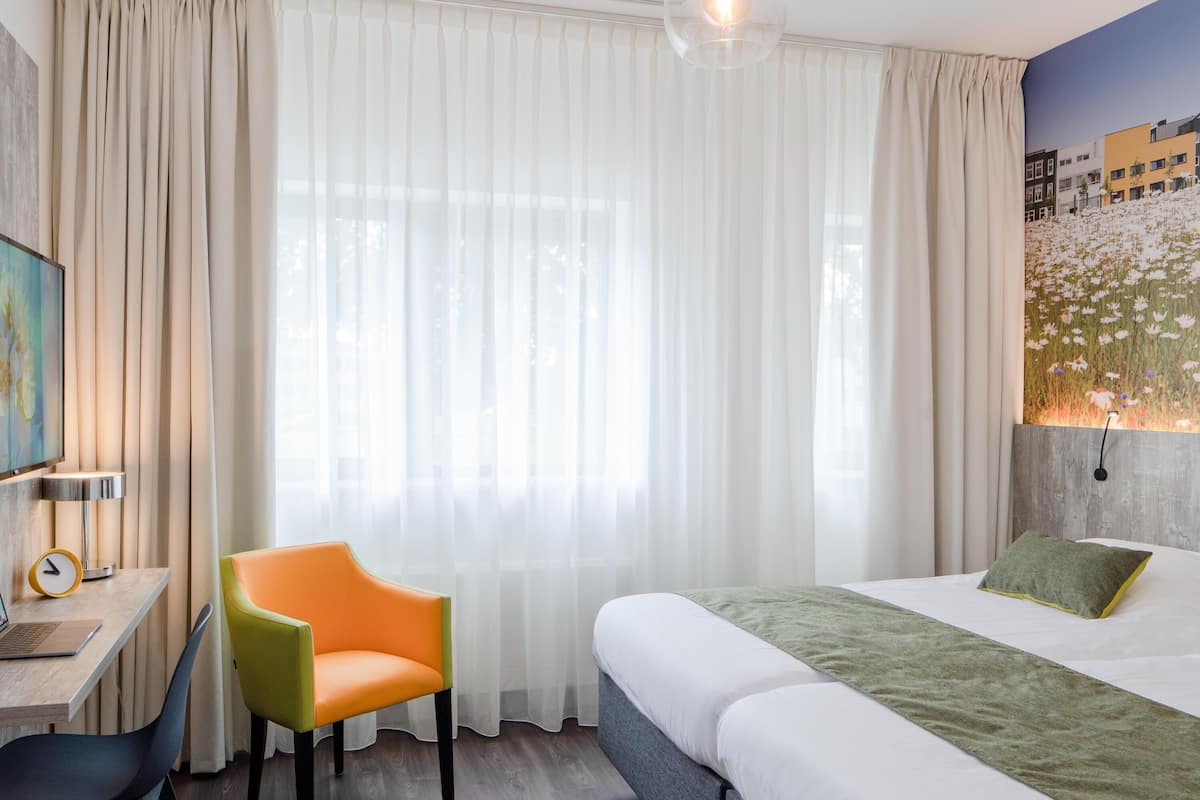 Una habitación de hotel con una cama, un escritorio, una silla y un cuadro en la pared.