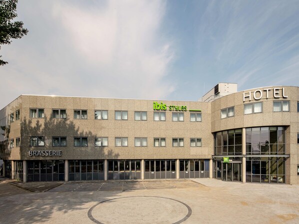A hotel with a modern design, featuring a 'Brasserie' and 'ibis styles' signage, and a spacious outdoor area.