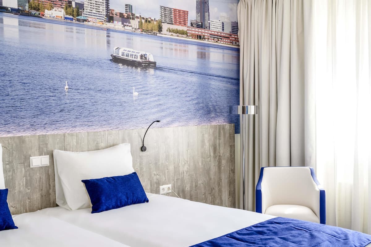 Habitación de hotel con cama, una silla, vistas a la ciudad y una ventana con cortinas.