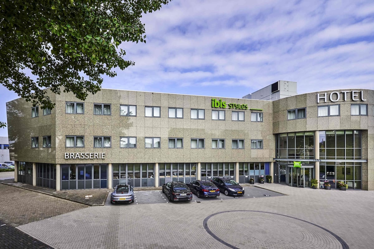 Un hotel de diseño moderno, con letreros de 'Brasserie' e 'Ibis Styles', varios espacios de estacionamiento y una zona de entrada pavimentada.