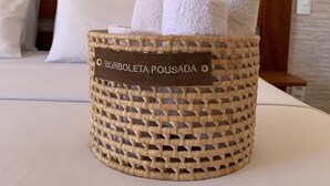 Ein gewebter Korb mit Handtüchern, auf denen "BORBOLETA POUSADA" steht, auf einem Bett in einem Hotelzimmer.
