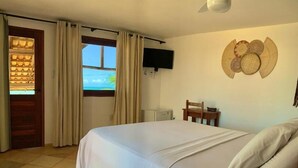 Ein Schlafzimmer mit einem Bett, einem Fernsehgerät an der Wand, einem Holzsessel und einem Fenster mit Vorhängen.
