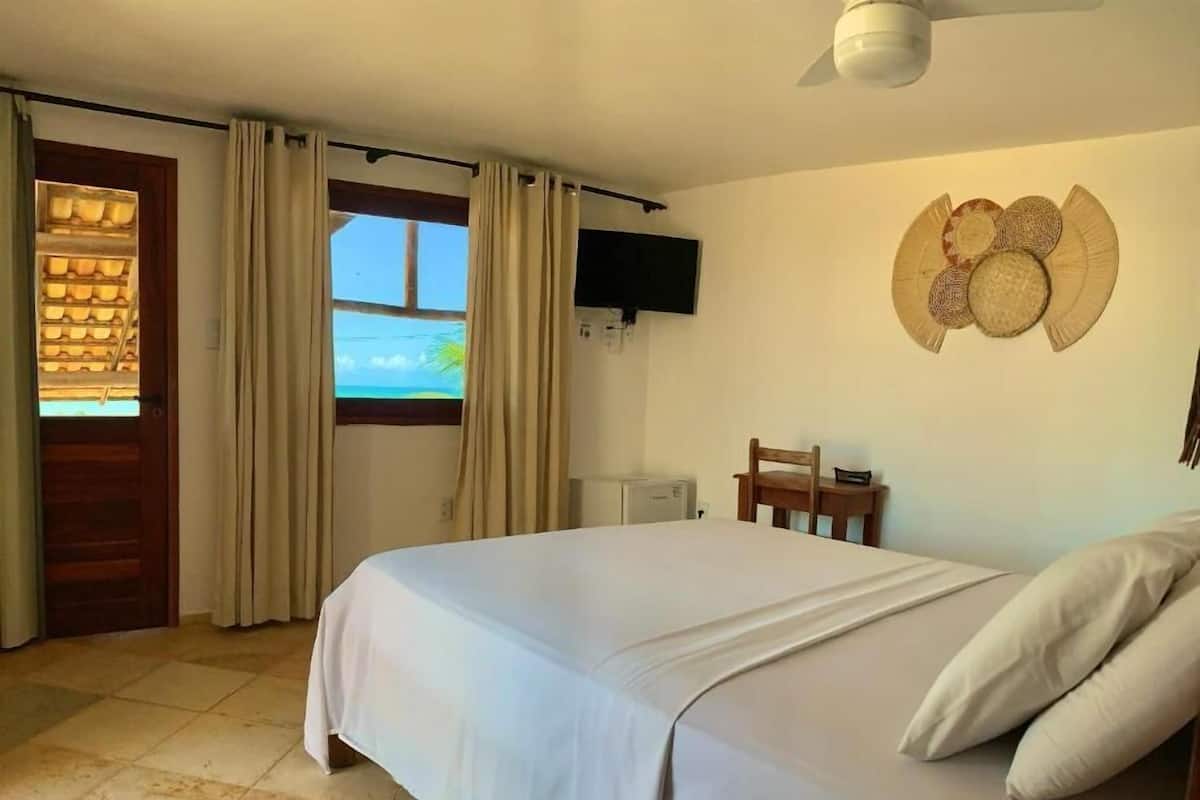 Ein Schlafzimmer mit einem Bett, einem Fernsehgerät an der Wand, einem Holzsessel und einem Fenster mit Vorhängen.