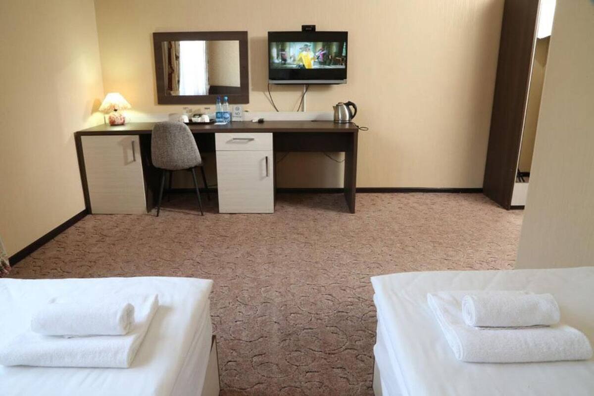 A hotel room with two beds, a desk with a chair, a television, and a small kitchenette.