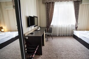 Habitación de hotel con cama, escritorio y silla, televisión y ventana con cortinas.