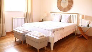 Une chambre bien rangée, avec un grand lit, deux tables de chevet, un miroir rond et un radiateur.