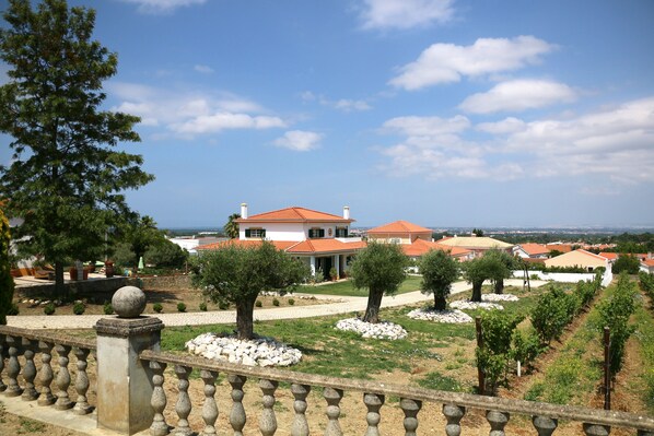 A villa with a red-tiled roof, surrounded by a landscaped garden with trees and a vineyard. - Quinta da Chapeleira. (Azeitão)