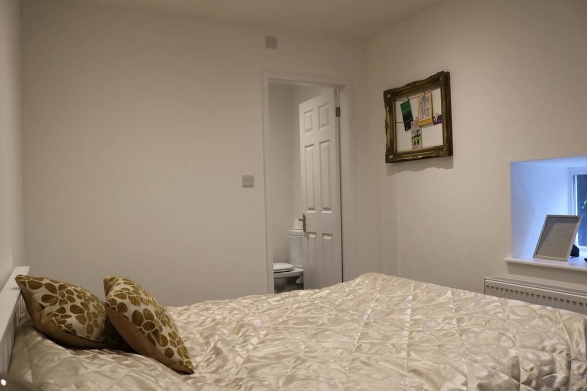 A bedroom with a bed, two pillows, a framed picture, and a window.