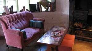 A cozy living room with a pink sofa, a wooden coffee table with magazines, and a fireplace with logs. - sweet heART Tea Rooms Accommodation (Harrogate)