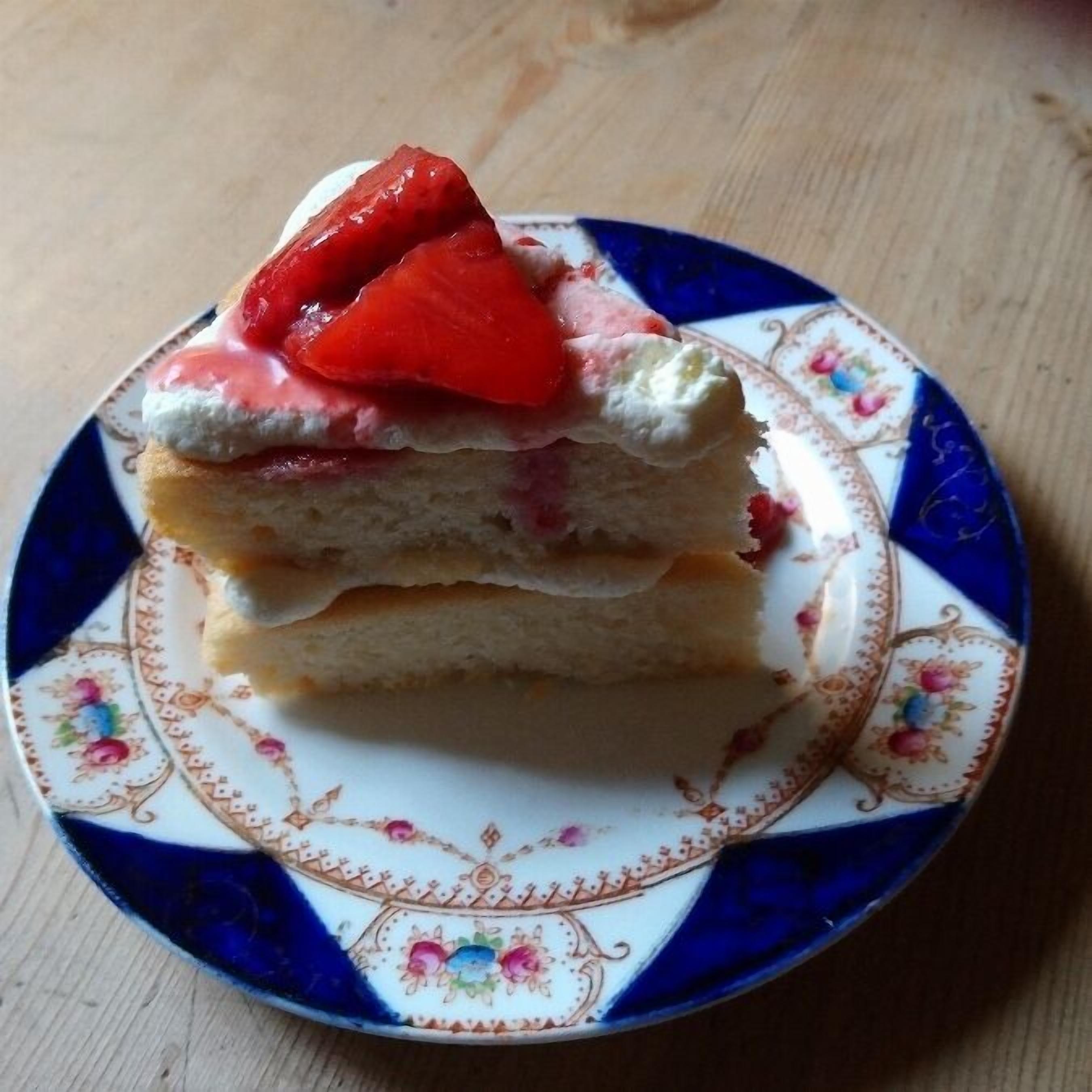 Une part de gâteau à plusieurs couches, garnie de fraises, présentée sur une assiette décorative.