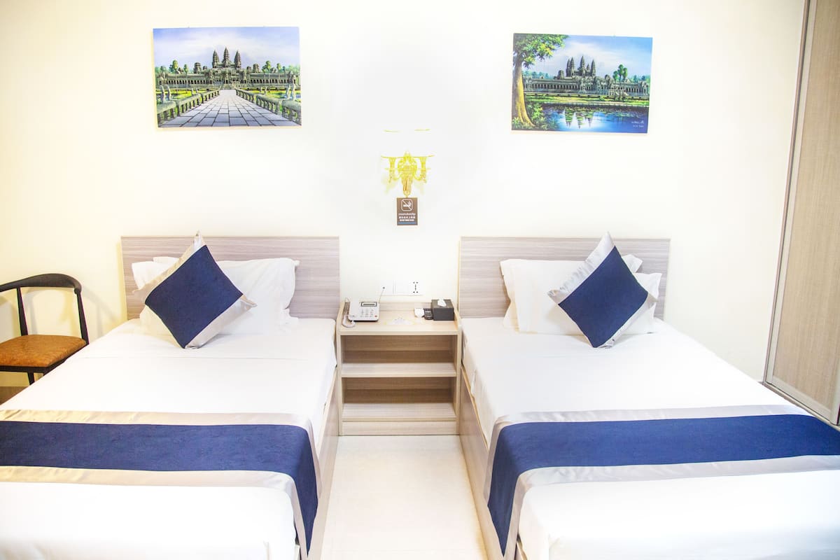 Une chambre d’hôtel avec deux lits, une chaise, une table de chevet avec un téléphone et deux tableaux encadrés au mur.