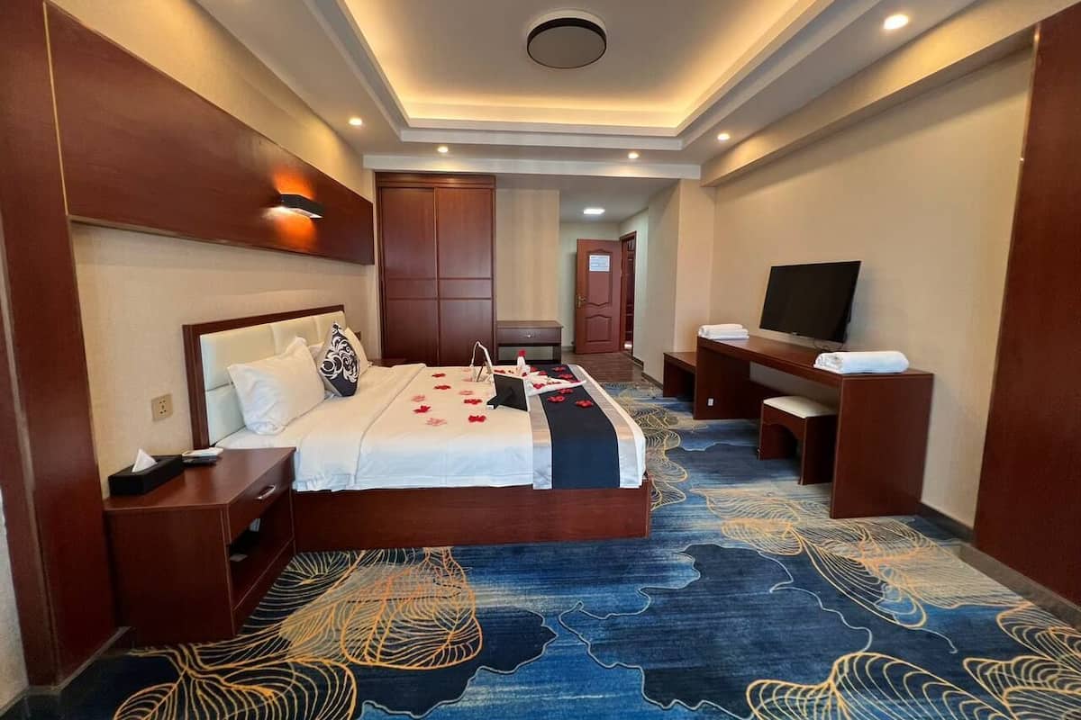 Une chambre d’hôtel avec un grand lit, un bureau, une télévision et une salle de bain visible à travers une porte ouverte.