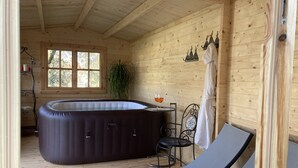 A wooden cabin with a hot tub, a lounge chair, a table with a glass of wine, and a window with a view of trees. - Vacation home with swimming pool and hot tub relaxation and tranquility (Lamporecchio)