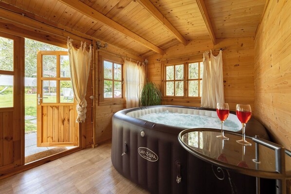 A wooden cabin with a hot tub, two glasses of red wine, and a view of the outdoors.