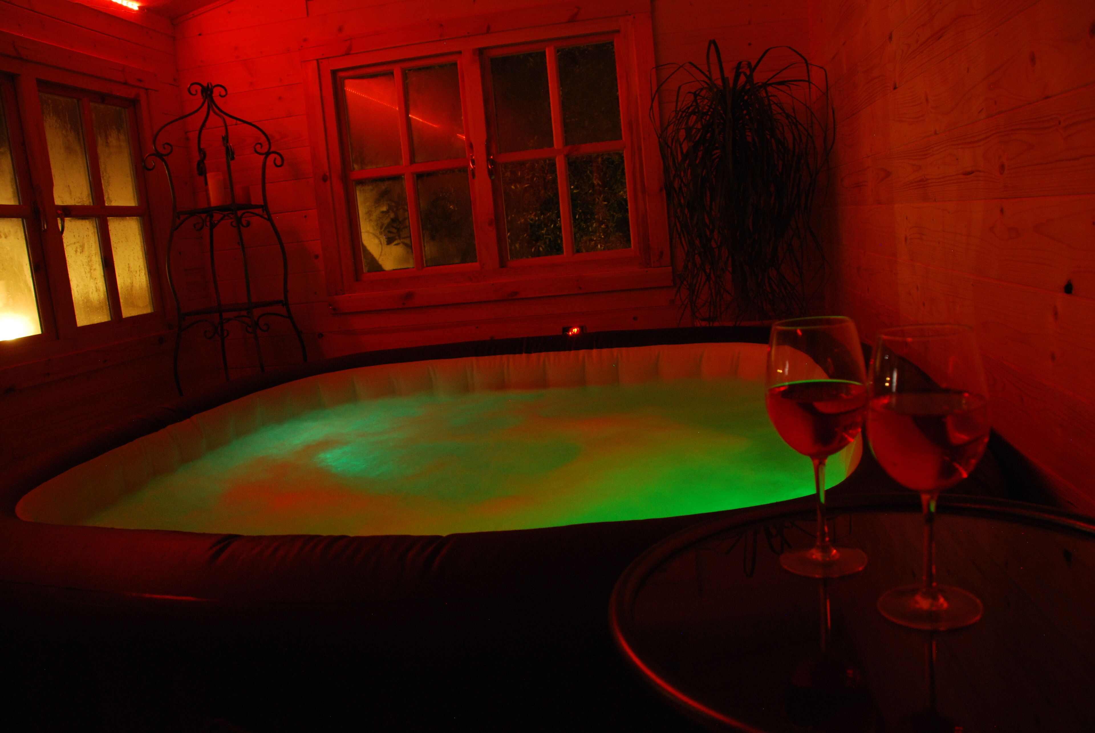 Um ambiente com pouca luz, piscina, dois copos de vinho sobre uma mesa e uma planta.