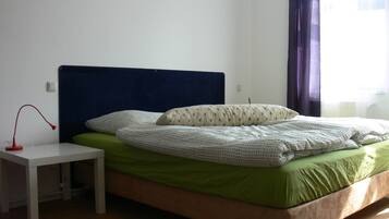 Una cama bien hecha con colchón verde y ropa de cama blanca, una mesita de noche blanca con una lámpara roja y un cabecero azul oscuro.
