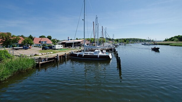 A marina with several boats docked, a small dock, and a few buildings in the background. - Gruppenhaus Rügen Zur Brunnenaue (Sagard)
