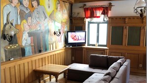A cozy living room with a large sofa, a wooden dining table, and a mural on the wall. - Gruppenhaus Rügen Zur Brunnenaue (Sagard)