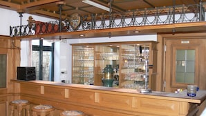 A bar area with wooden stools, a glass display case with glasses, and a sign reading "Küche". - Gruppenhaus Rügen Zur Brunnenaue (Sagard)