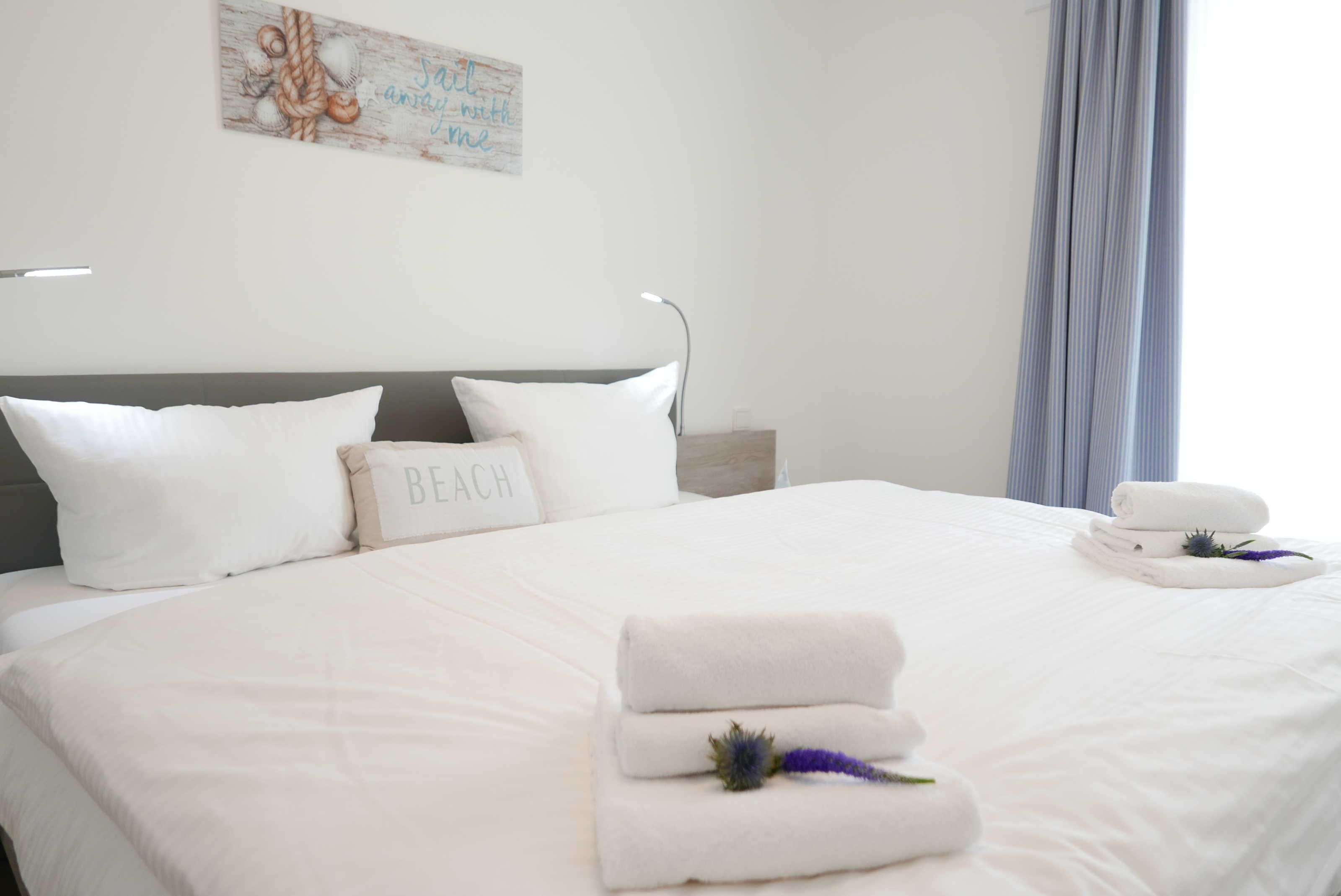 Una cama bien hecha con sábanas blancas y una almohada con la etiqueta "BEACH".