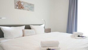 A neatly made bed with white linens and a pillow labeled "BEACH".