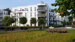 A modern multi-story building with balconies, a landscaped garden, and a clear sky.