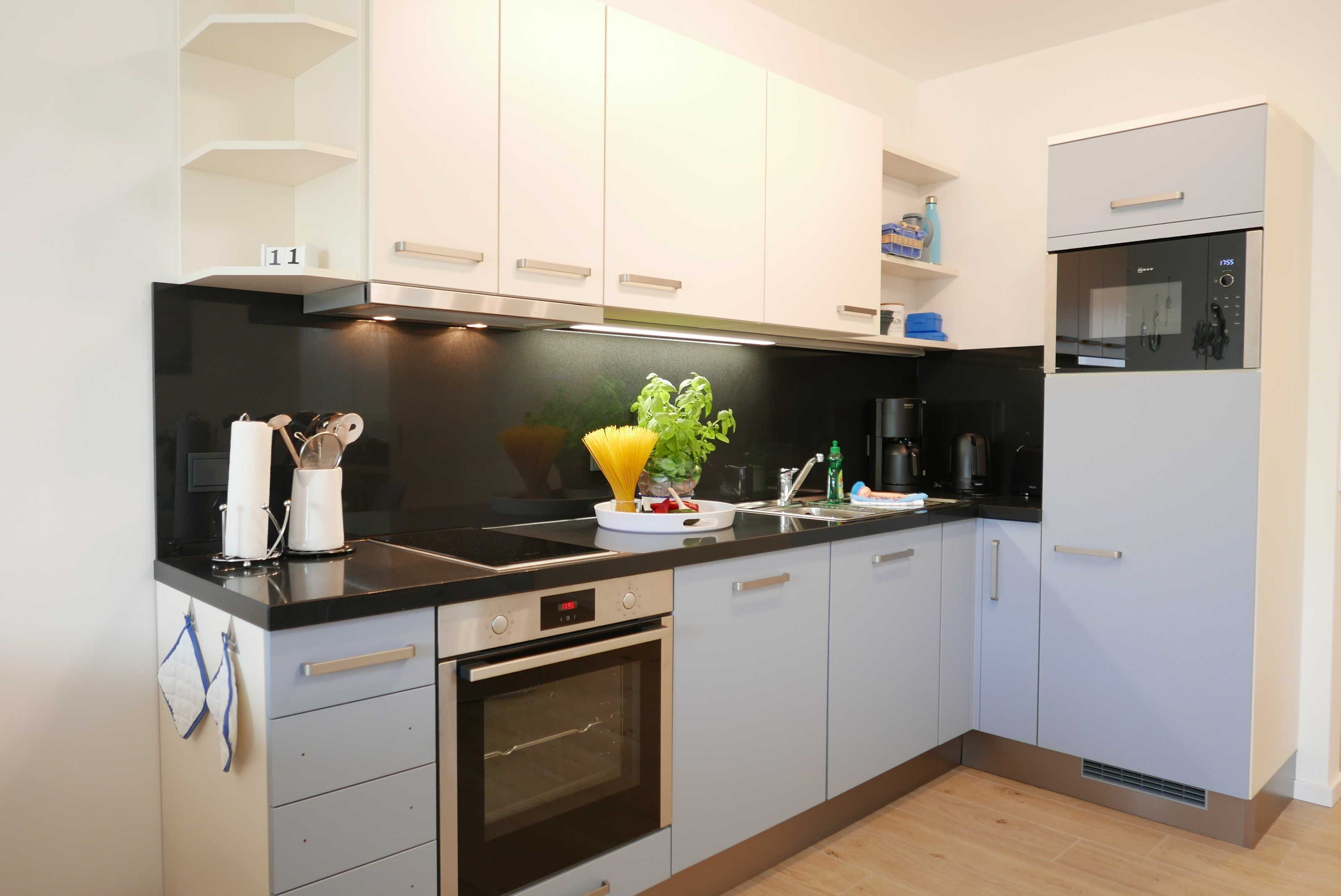 A modern kitchen with white cabinets, a black countertop, and stainless steel appliances including an oven and a coffee maker.