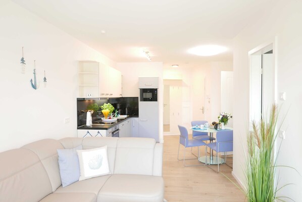 Ein modernes Wohnzimmer mit einer Couch, einem Essbereich mit Tisch und Stühlen sowie einer Küche mit Geräten.