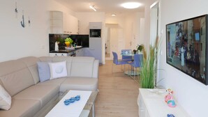 A modern living room with a beige sofa, a coffee table, and a dining area with blue chairs.