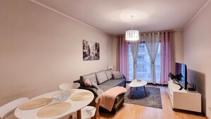 A modern living room with a sofa, dining table, chairs, a TV, and a window with curtains. - Platane (CH10) - CH10 (Swinoujscie)
