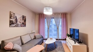 A modern living room with a grey sofa, a white coffee table, a TV on a white cabinet, and a cityscape painting on the wall. - Platane (CH10) - CH10 (Swinoujscie)