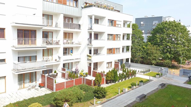 A multi-story residential building with balconies, a landscaped garden, and a pedestrian pathway. - Platane (CH10) - CH10 (Swinoujscie)