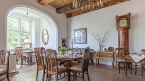 A dining area with wooden chairs and a table, a large mirror, a chandelier, and a grandfather clock. - Apartment 4 Anna Owena (ID 386) (Oldenswort)
