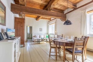 Un comedor con una mesa y sillas de madera, un televisor sobre un mueble, y vista del salón contiguo.