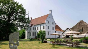 A large white building with a red roof, surrounded by a grassy area with outdoor seating. - Apartment 4 Anna Owena (ID 386) (Oldenswort)