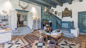 A lobby with a checkered floor, a staircase with blue railings, a chandelier, and a wall-mounted deer skull. - Apartment 4 Anna Owena (ID 386) (Oldenswort)