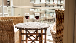 Una mesa de mimbre con dos copas de vino tinto en un balcón con vista a un edificio residencial.