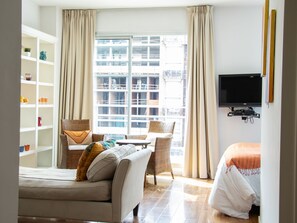A modern hotel room with a sofa, a chair, a TV, a bookshelf, and a large window with curtains. - Cabrera Modern Flat (Buenos Aires)
